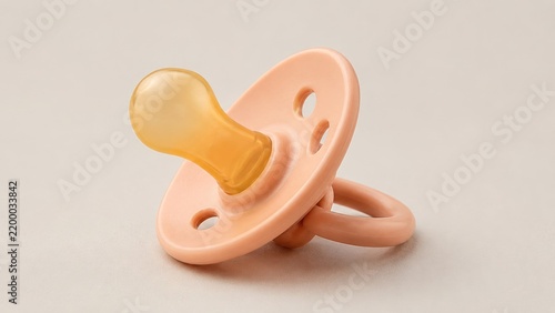 Peach silicone baby pacifier with rounded nipple on a neutral beige background, isolated infant comfort and feeding accessory