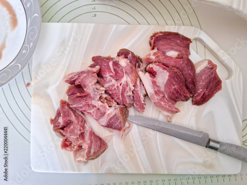 Konstfotografi Fresh raw pork meat sliced with knife on white artificial stone cutting board next to ceramic plate and board stand high angle view