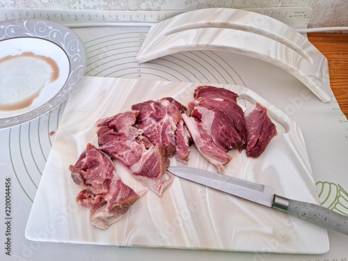 Obraz na płótnie Fresh raw pork meat sliced with knife on white artificial stone cutting board next to ceramic plate and board stand high angle view