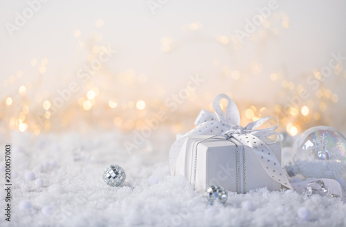 White Christmas gift box in snow with silver ornaments and warm golden bokeh for New Year greeting card or holiday advertising