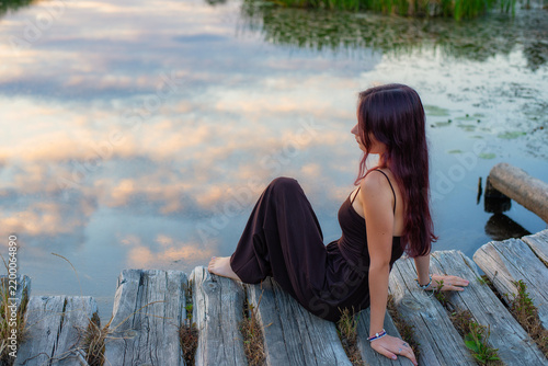 Young woman sitting on a weathered wooden pier by a calm lake during a peaceful golden sunset