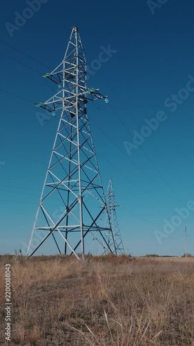 High voltage power poles and cables with steel supports in the field, vertical video.