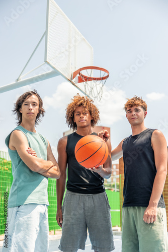 vertical Multicultural male friends posing with basketball on court