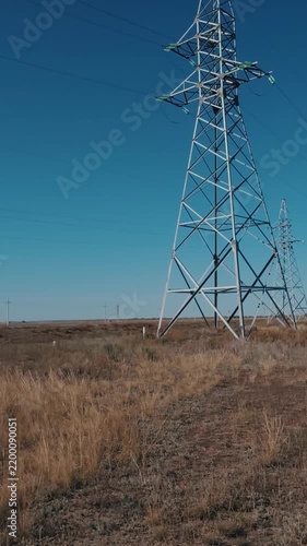 High voltage power poles and cables with steel supports in the field, vertical video.