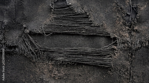 Torn dark distressed fabric texture with exposed horizontal frayed threads and dirt