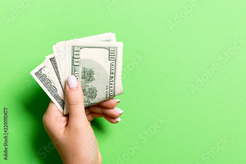 Top view of female hand holding a pack of money on colorful background. One hundred dollars. Business concept with empty space for your design. Charity and tips concept