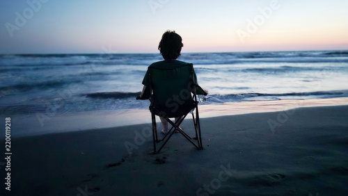 Canvastavla Person Sitting on Camping Chair on Beach Watching Ocean Waves at Dusk in Contemplation