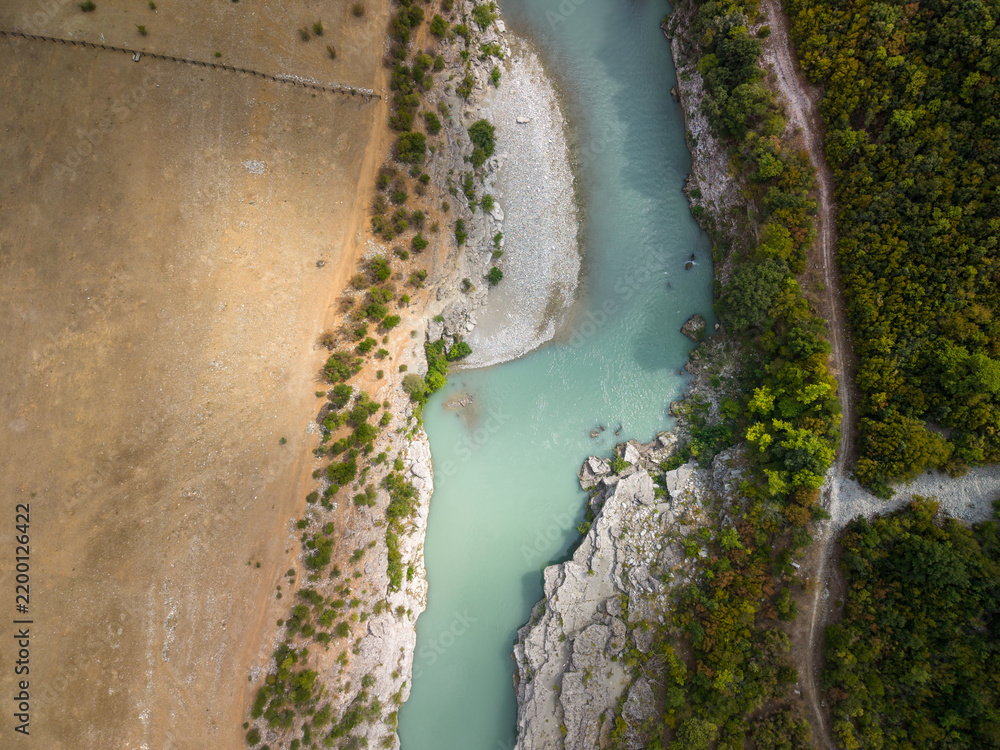 Fototapeta premium Vjosa River passes narrow canyon in Albania. Overhead perspective shows pale blue current, stony banks and green woodland, with serene wilderness character and vivid color contrast.