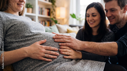 Pregnant surrogate mother with intended parents touching belly in modern room