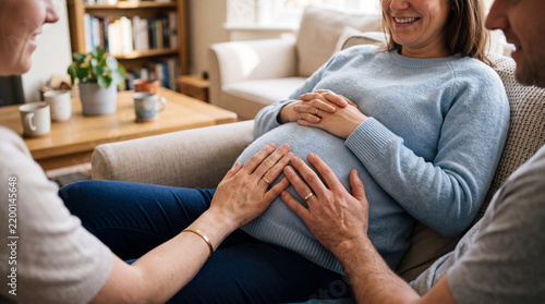 Pregnant woman sitting on a couch with supportive couple touching her belly