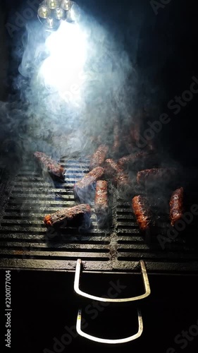 traditional Romanian skinless grilled sausages sizzling on a charcoal barbecue with thick smoke rising under a flashlight with a white smoke rising from the heat