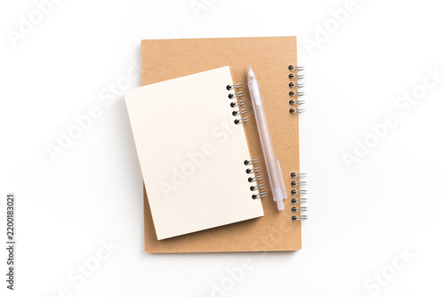 Top view of small blank spiral notebook stacked on kraft paper notebook with two pens on white background with copy space