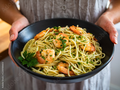 Woman holding spaghetti bowl with fried shrimps, olive oil and parsley 