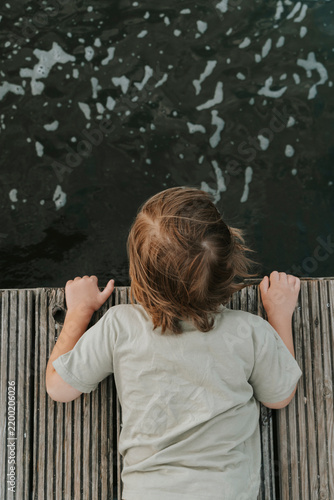 Child Looking Down at Dark Water from Wooden Dock