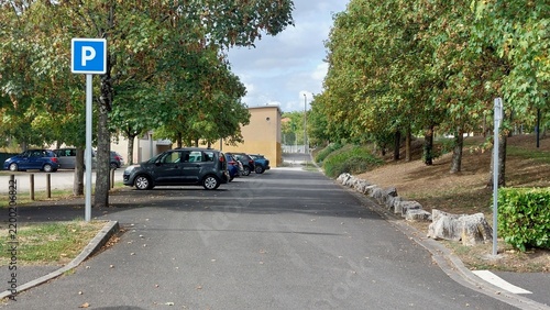 Panneau carré parking à l'entrée d'une aire de stationnement ombragée.