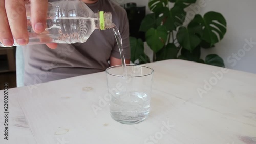 Man's hand pouring clean drinking water from a plastic bottle into a transparent glass at home