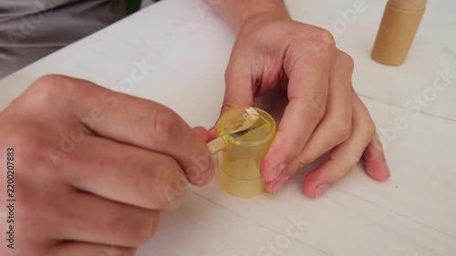 Male hands carefully sharpening a classic wooden pencil with a yellow manual sharpener