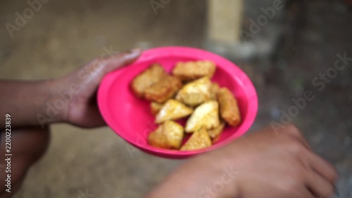 A person's hand holding a red plate filled with warm fried tempeh and tofu, serving a protein-rich traditional Indonesian soybean dish for culinary concepts.