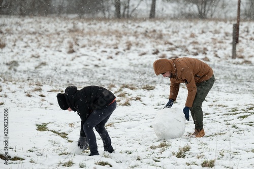 Картината върху платно Two individuals build a snowman together in a snowy field, enjoying a winter day's playful activities