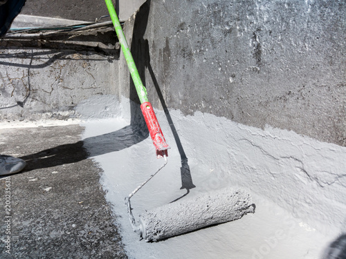 Worker applying liquid membrane with a roller on a flat roof for waterproofing