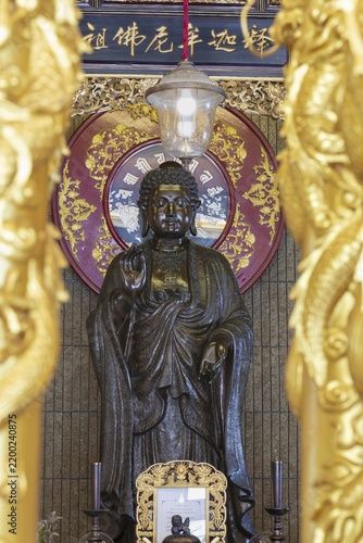 A standing Buddha in front of a richly decorated red mandala radiates quiet dignity and timeless serenity, golden pillars frame the scene like a gateway to inner contemplation and spiritual peace, Chee Chin Khor Temple, Bangkok, Thailand