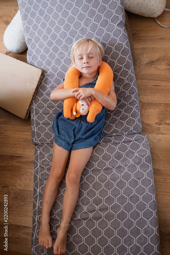 Fotografie little girl sleeping peacefully on folding mattress holding orange travel neck