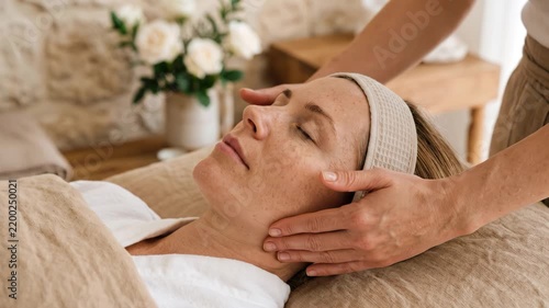 Professional masseuse performing relaxing facial skincare massage for woman lying in cozy spa resort