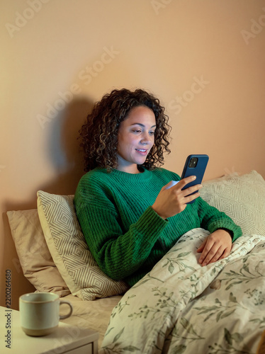 Smiling Woman in Green Sweater Relaxing in Bed Using Smartphone