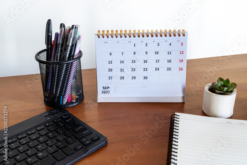 Desktop desk calendar for September 2027 surrounded by keyboard, pen holder, succulent plant, and notebook on wooden table.