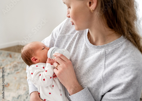 Foto Caring mother feeds tiny newborn baby with milk bottle inside bright home during