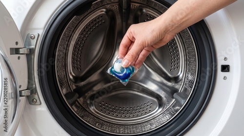 Close up of a hand holding a blue laundry detergent capsule in front of an open washing machine