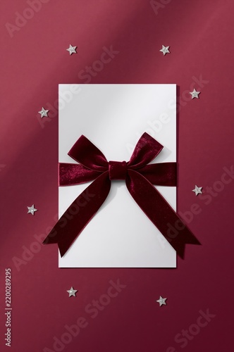 Gift With Red Bow and Silver Stars on a Burgundy Background