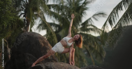 Young Woman Practicing Yoga on Tropical Rocks at Dusk