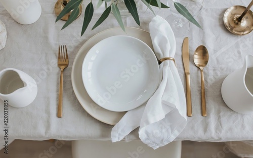 Table setting with white plates, gold cutlery, and greenery dinnerware