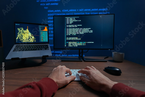 First person view of a programmer hands typing on a keyboard at night, two monitors displaying code and data science visualizations on dark desk, works on a machine learning or data science. POV
