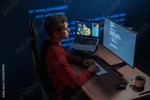 Concentrated data scientist typing code in a dimly lit workspace, multiple screens filled with programming code and data. Focused developer works late at night on a machine learning and ai project. 