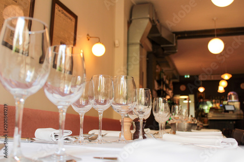 Bild auf Leinwand Line of empty wine glasses aligned on white tablecloth in traditional French brasserie interior with warm ambient lights and bokeh background