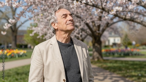 A joyful Black man stands beneath blooming cherry trees in a vibrant spring park, surrounded by colorful tulips and soft sunlight.