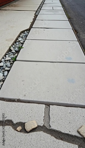 Weathered cement sidewalk with aggregate rocks, gray tones, weathered surface.
