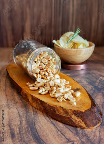 Peanuts spilling from jar with potato chips and rosemary