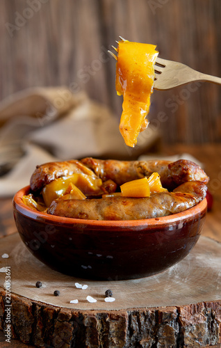 Sausages with yellow peppers in terracotta bowl