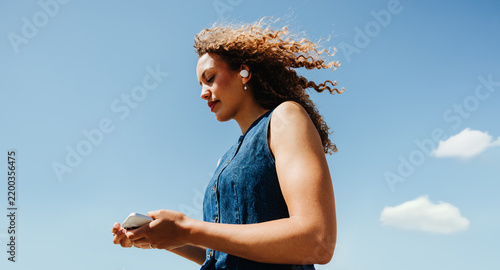 Checking smartphone while listening with earPods under clear blue sky