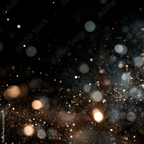 Microscopic particles float against a dark background creating an ethereal depth of field effect. Warm amber and cool blue bokeh circle shapes vary in size and glow softly.