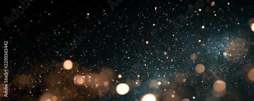 Floating particles create a dynamic dust cloud effect in motion. Golden and blue bokeh lights blend softly with scattered fine specks. This atmospheric image suits backgrounds and abstract.