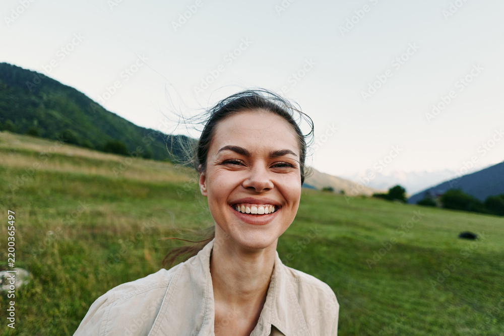 Fototapeta premium Smiling woman outdoors enjoying nature, close crop over a grassy field with hills, conveying wellness and lifestyle through warm natural light.