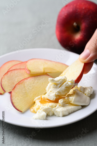 Hand holding sliced red apple and dipping into cream cheese with honey on a white plate, Healthy eating