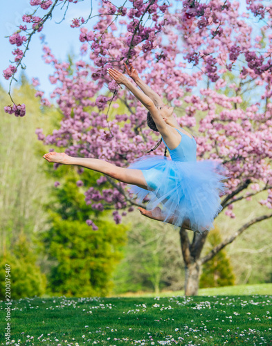 Ballet white dancer leaping near flowering tree outdoors in spring