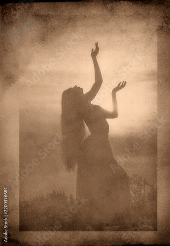 Silhouette of white woman dancing outdoors at sunset in sepia tone