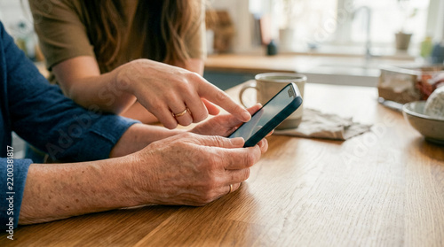 Young Woman Helping Senior Mother Use Smartphone at Kitchen Table