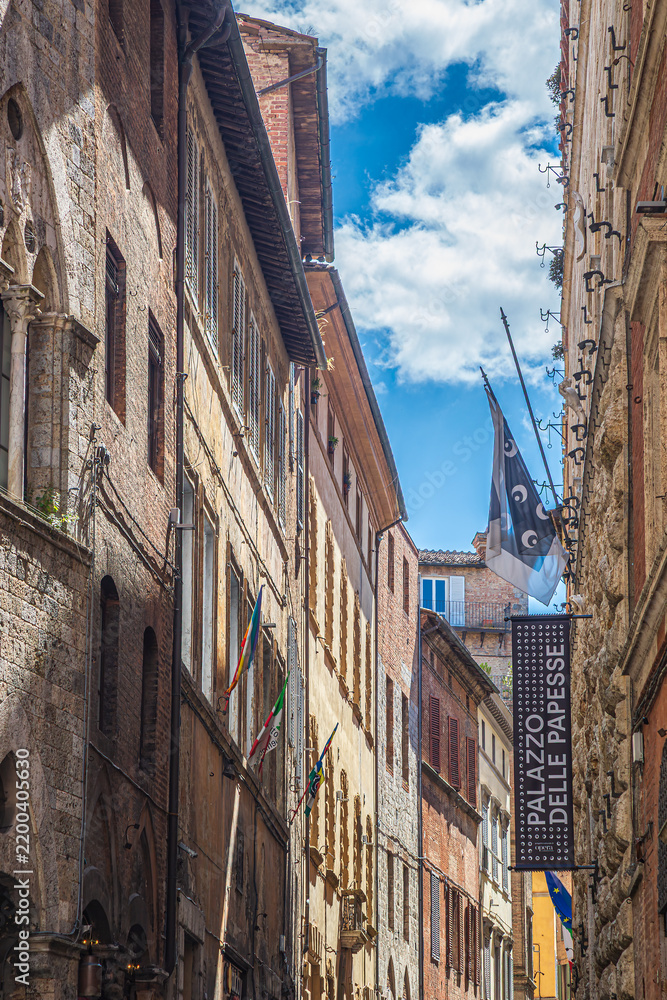 Obraz premium Siena, Italy - 23 may 2026: A narrow street in the historic center of Siena, Italy, featuring a vertical sign reading 